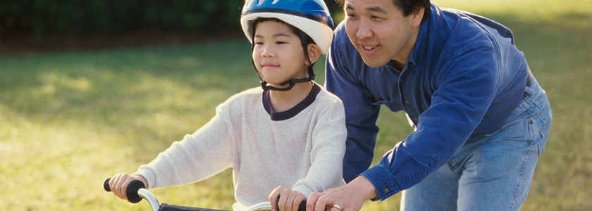 Dad holds onto the back of a bike as his sons learns to ride without training wheels